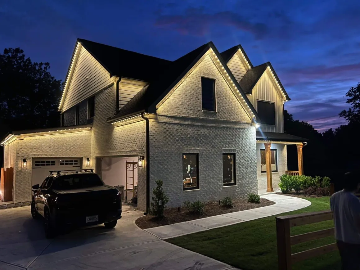 Large white-brick home with warm-white permanent roofline lighting